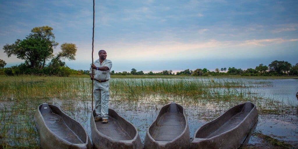 man standing in mokoro on Okavango Delta